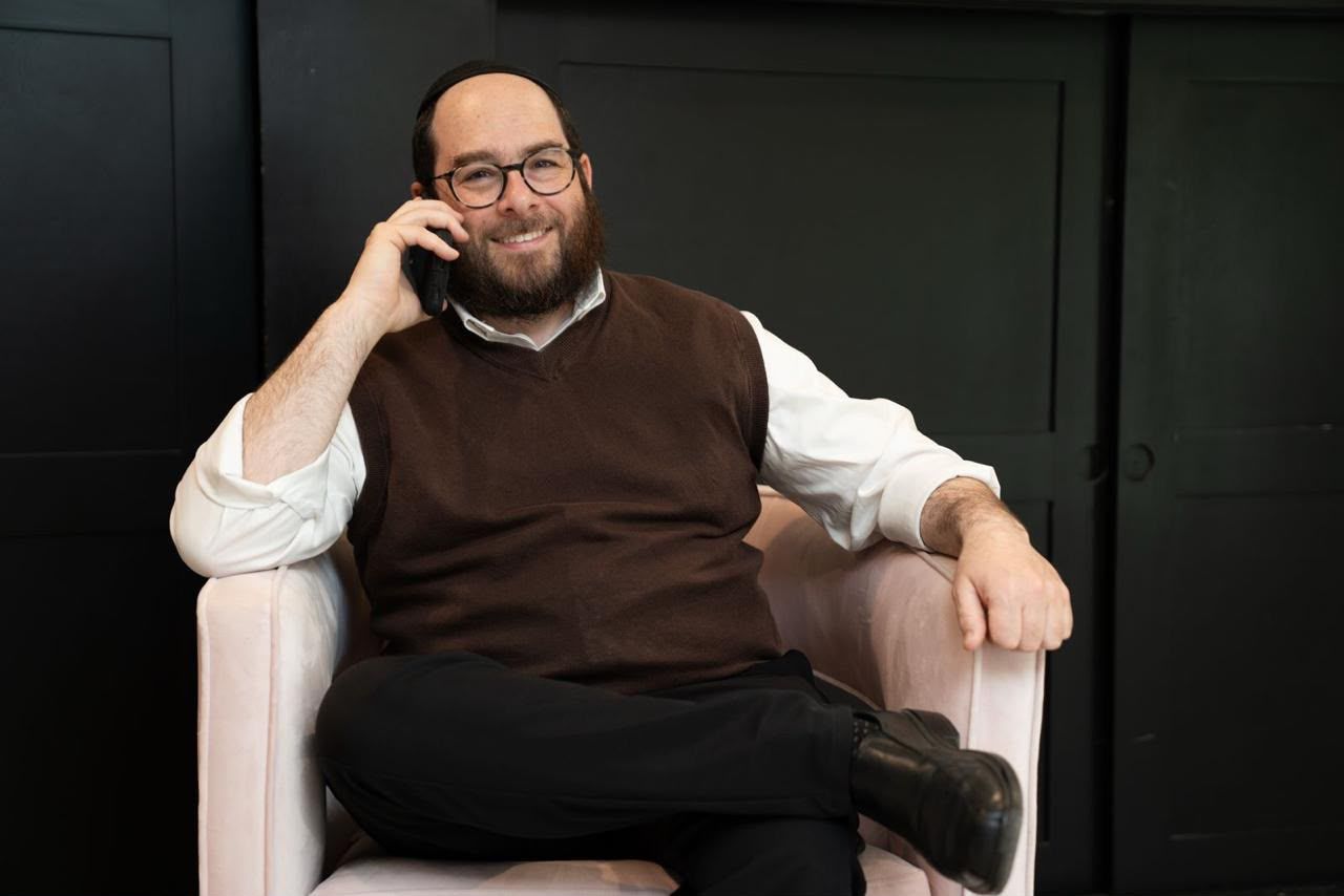 Naftali Smith smiling on a phone call, sitting in an armchair