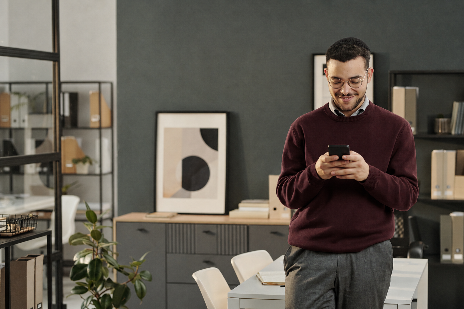 A young man smiling as he reads on his phone in an office